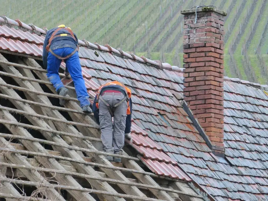 Two roofers working on a tiled roof beside a brick chimney
